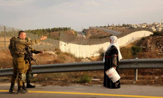 A Palestinian woman talks to an IDF military man in his olive fields on the other side of the Israeli separation wall, after obtaining special Israeli permission to pick olive trees in Hebron, West Bank, Photo: Hazem Bader/AFP